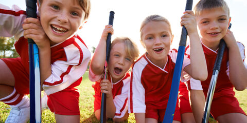 Portrait of happy children playing field hockey.