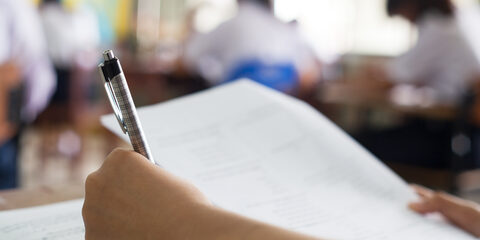 Close up hand of students reading and taking exam sheets exercises answer with stress in classroom