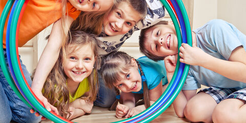 Five cheerful kids looking through hula hoops