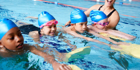 Female Coach In Water Giving Group Of Children Swimming Lesson In Indoor Pool